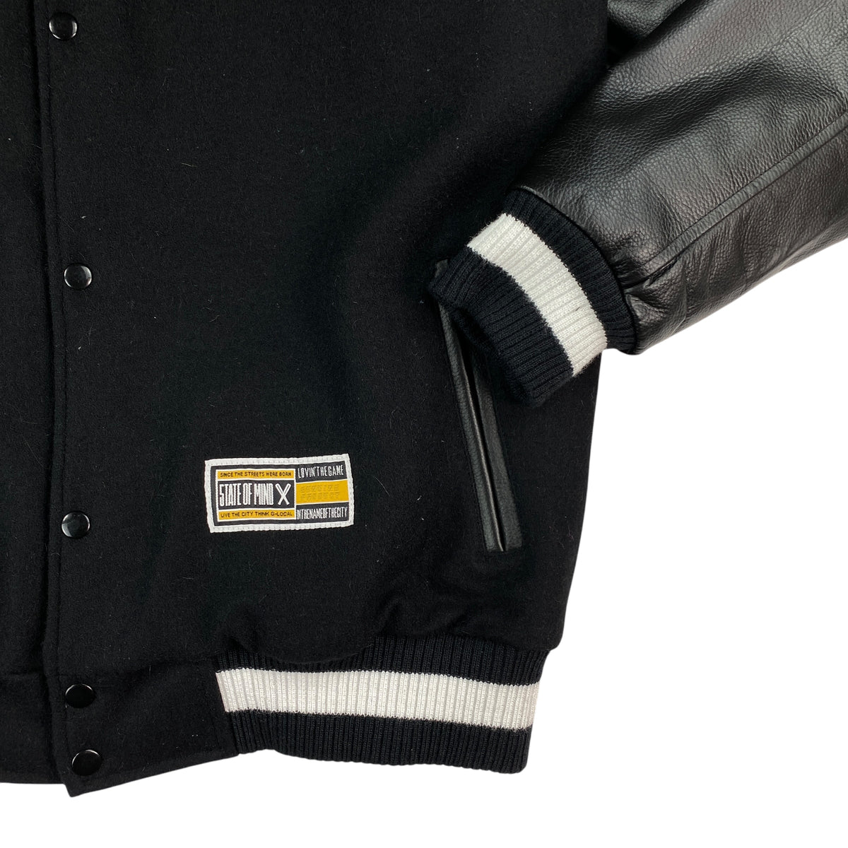 Fianco della giacca varsity State of Mind con tasca laterale a filo, etichetta logo e polsino in costina a righe