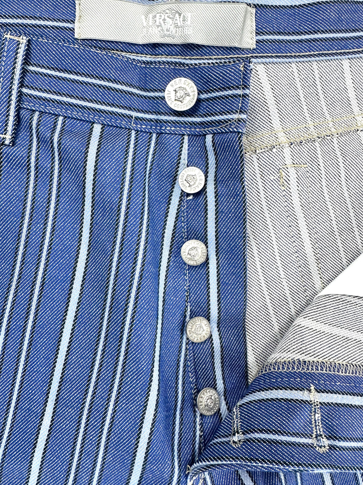 Chiusura frontale del jeans aperta, con i bottoni metallici a vista in fila