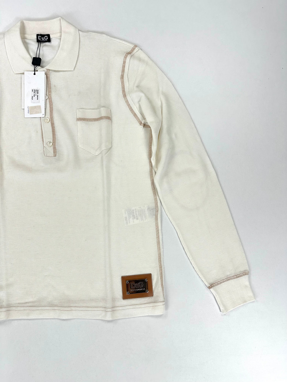 Polo panna D&G distesa di tre quarti, con il cartellino originale applicato alla spalla