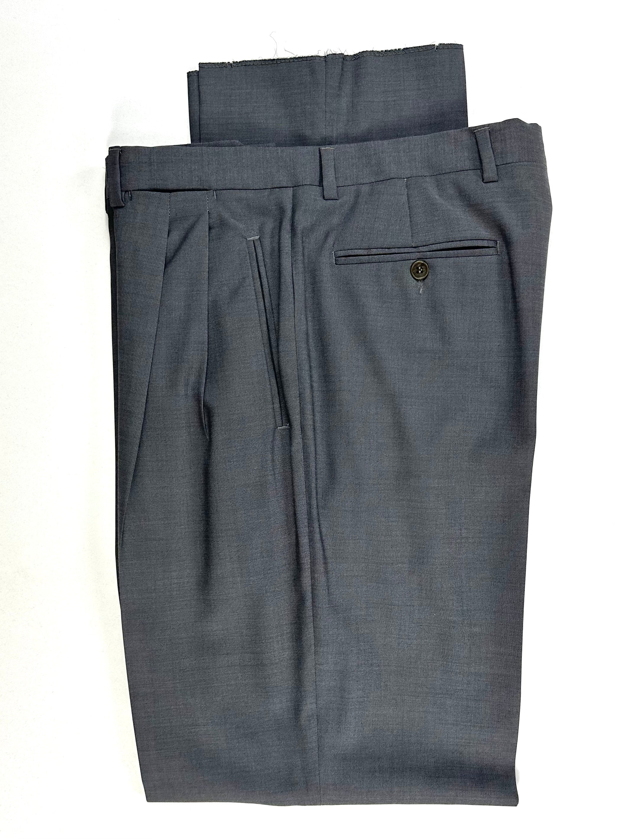 Dettaglio del pantalone piegato: vita, passanti e tasca posteriore a filetto con bottone
