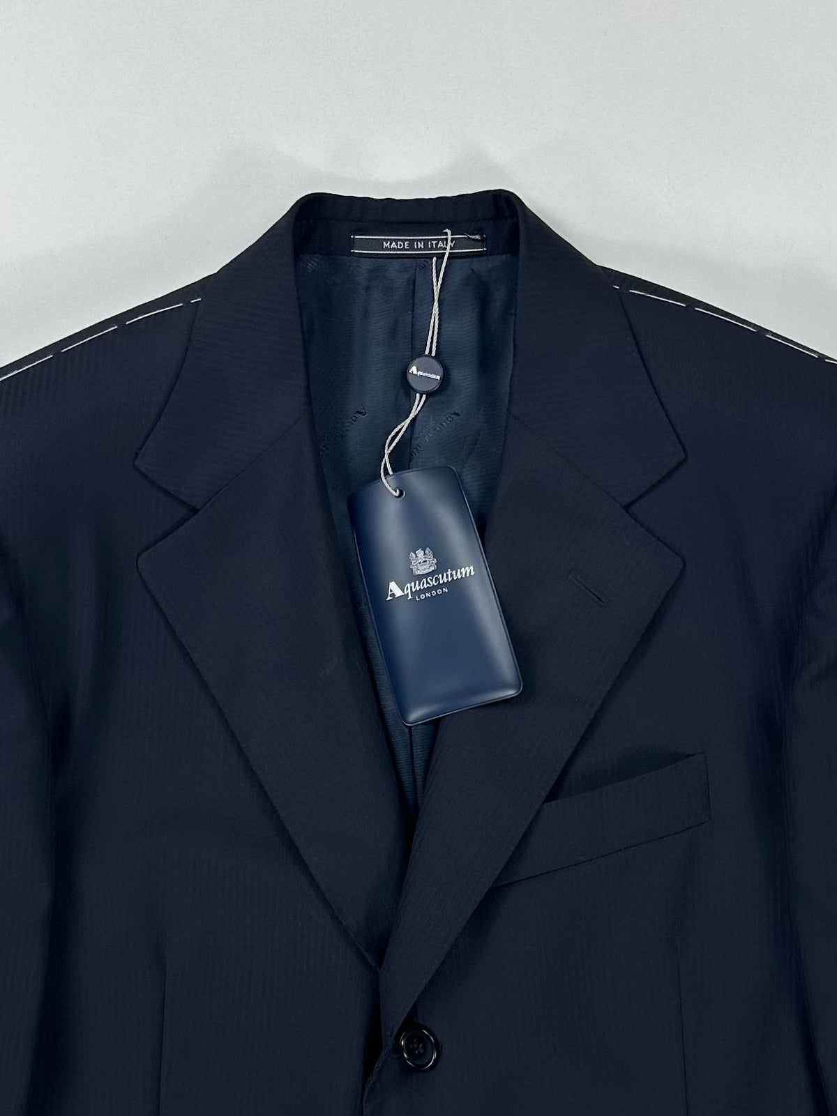 Parte alta della giacca Aquascutum: revers a dente, taschino a filetto e cartellino appeso