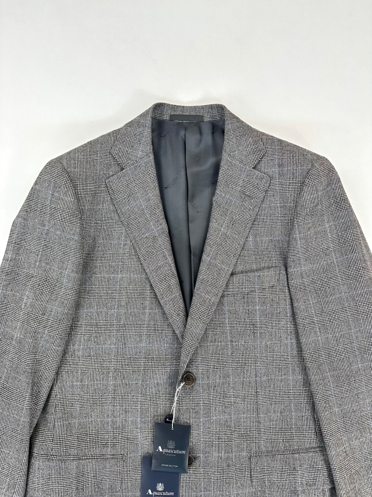 Parte alta della giacca Aquascutum: revers a dente, collo e cartellino con bottone di scorta