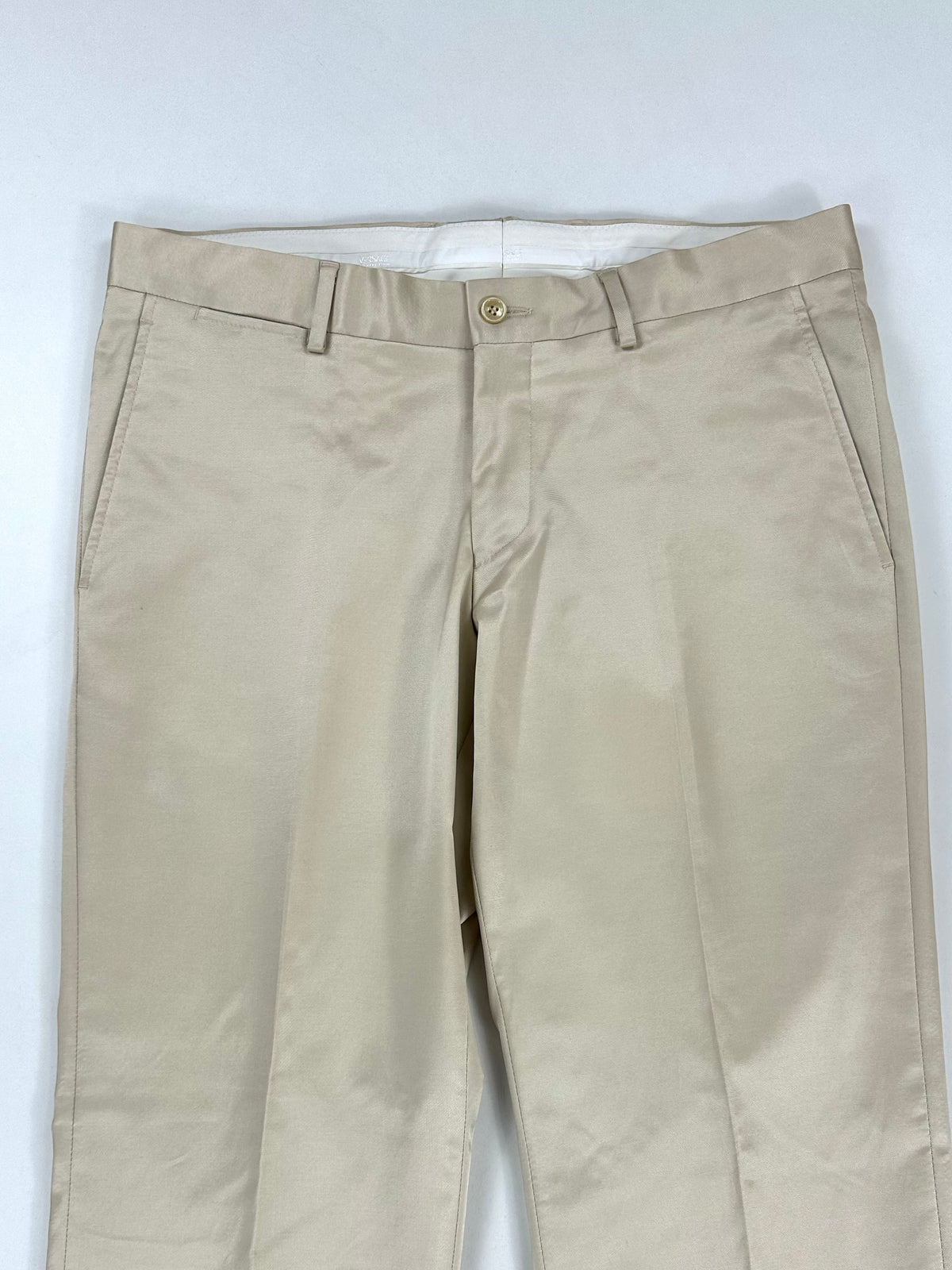 Parte alta del pantalone panna: passanti in vita, chiusura a bottone e tasche laterali oblique