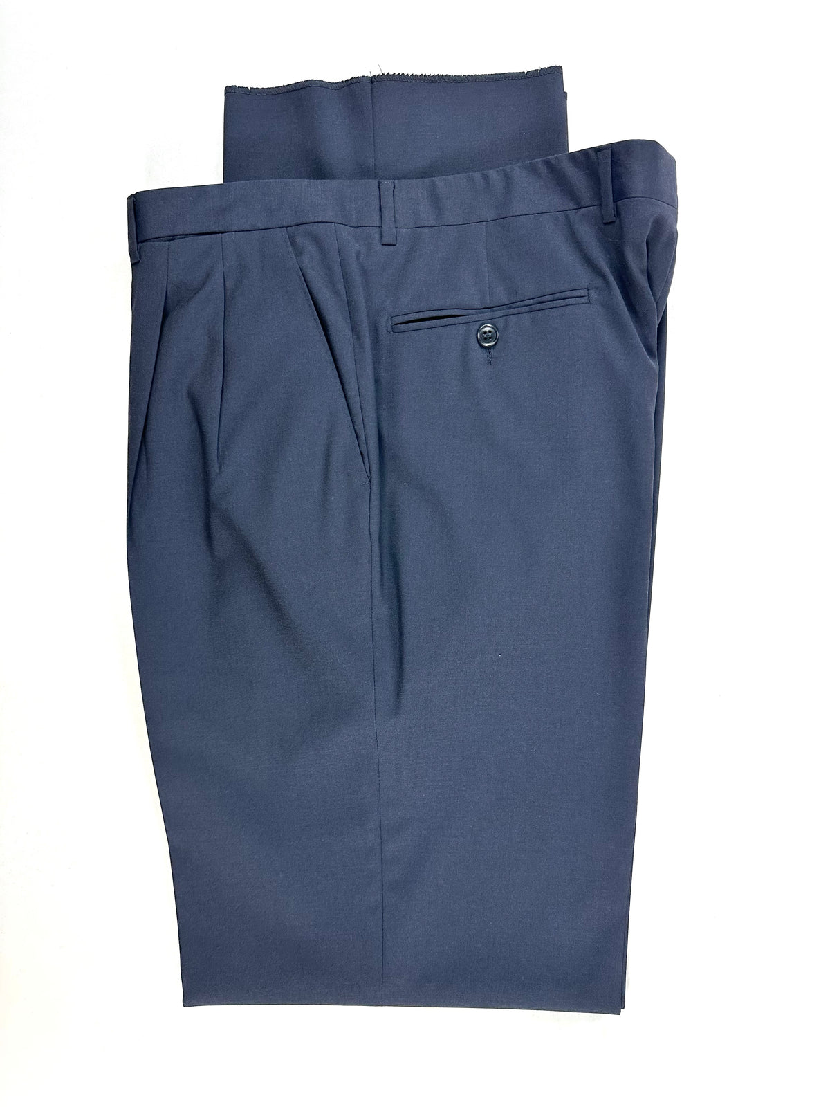 Dettaglio del pantalone piegato: vita, passanti e tasca posteriore a filetto con bottone