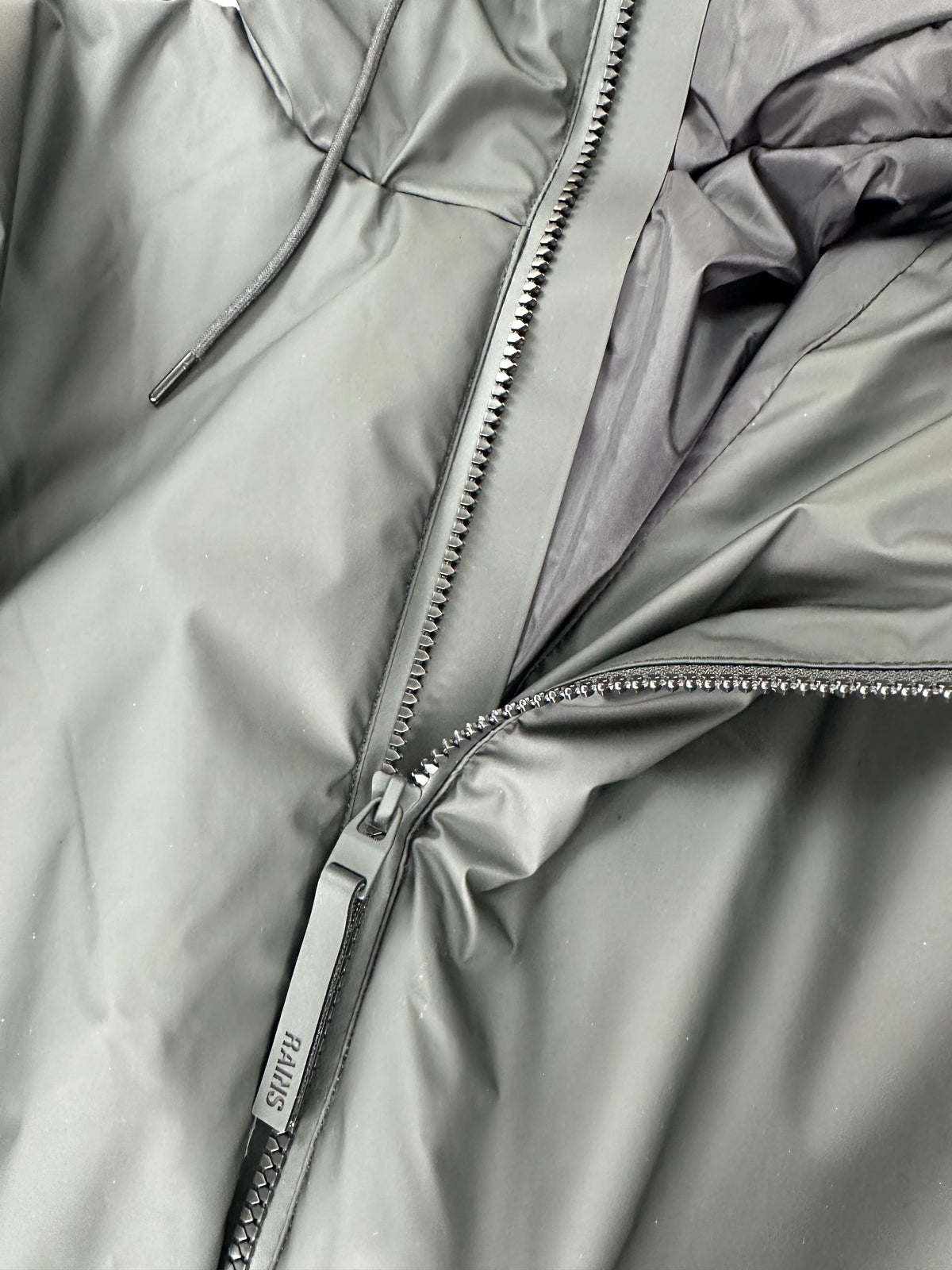 Dettaglio della zip frontale coperta della giacca Rains nera